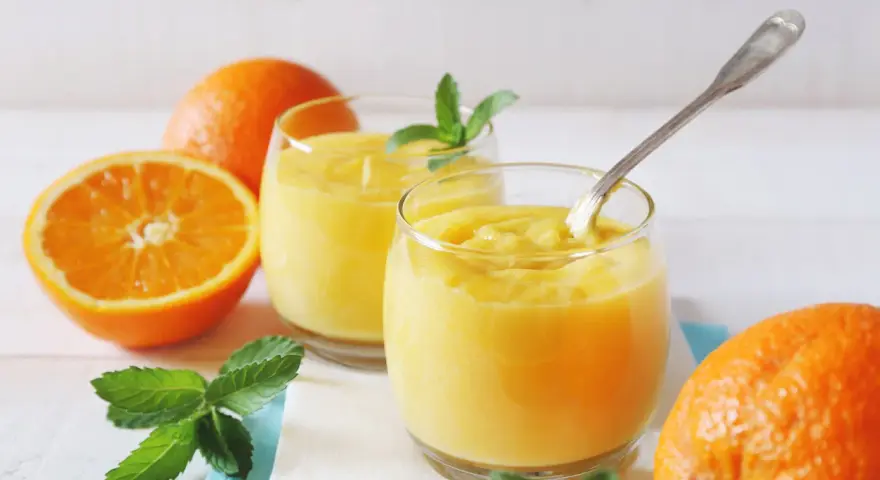 Dwa szklanki orzeźwiającego, gęstego **orange curd** z miętą i świeżymi pomarańczami.