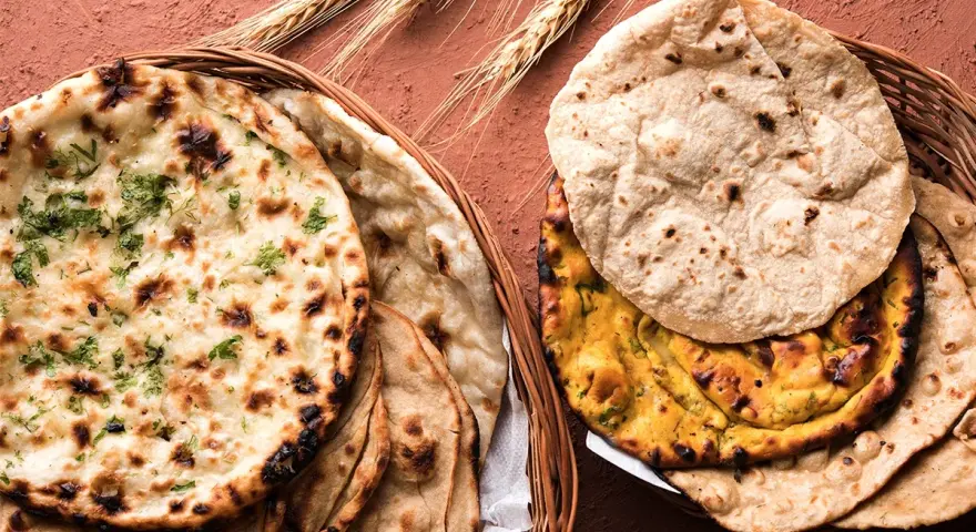 Dwa koszyki pełne pysznego chleba indyjskiego, w tym aromatyczny naan z kolendrą i klasyczny roti, ozdobione kłosami zboża.