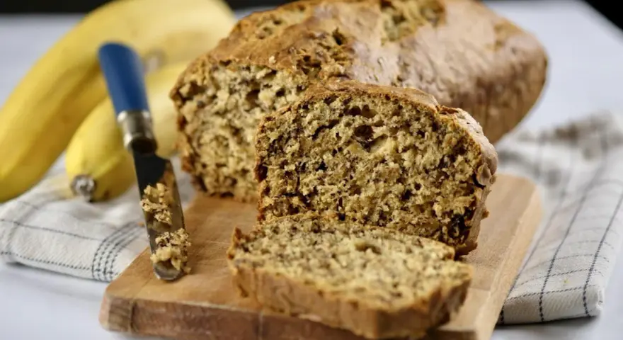 Pyszny chlebek bananowy, świeżo upieczony, z widocznym nożem i bananami w tle. Idealny na śniadanie.