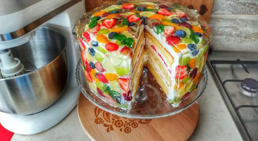 Kolorowy tort z galaretką i owocami, z kawałkiem wyciętym, prezentuje się apetycznie.