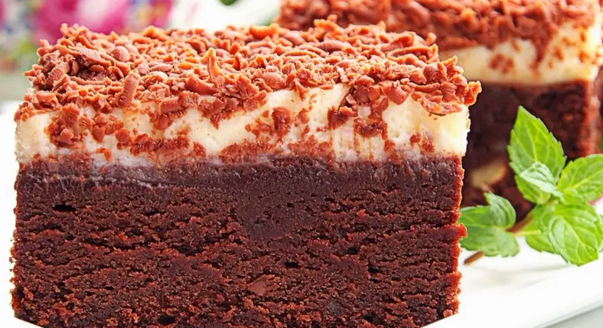 Pyszny torcik brownie z kremową warstwą i posypką czekoladową, ozdobiony listkami mięty.