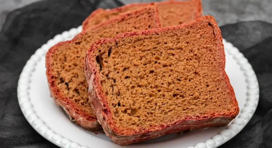 Kilka kromek pysznego, domowego chleba buraczanego na białym talerzu.