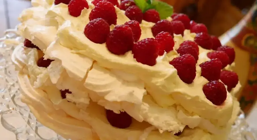 Puszysty, wielowarstwowy tort bezowy z bitą śmietaną i malinami. Wygląda jak najpyszniejszy tort bezowy, jaki można sobie wyobrazić!
