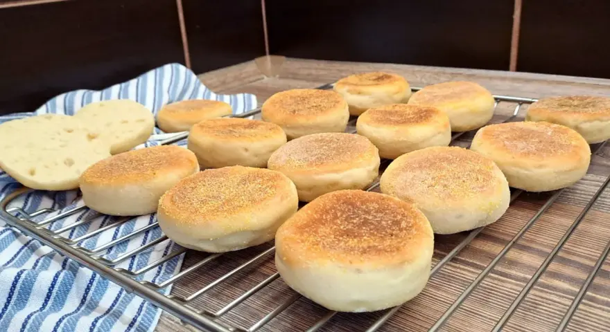 Świeżo upieczone muffiny angielskie, lekko zrumienione, czekają na śniadanie. Dwa przekrojone bułeczki odsłaniają puszyste wnętrze.