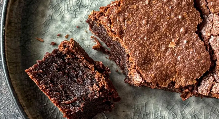 Pyszne, wilgotne brownie bezglutenowe na popękanym, szarym talerzu. Kawałek z widelcem czeka na spróbowanie.