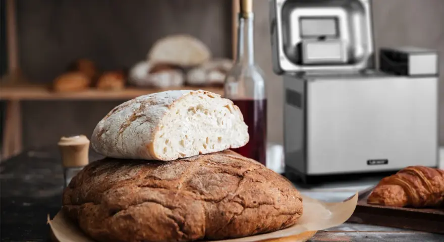 Chrupiący chleb z automatu, świeżo upieczony, czeka na śniadanie. Obok butelka wina i croissant.