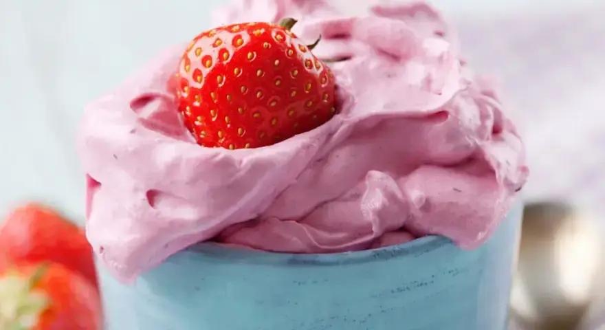 Puszysty mus truskawkowy w niebieskim naczyniu, ozdobiony świeżą truskawką. Idealny deser na lato.