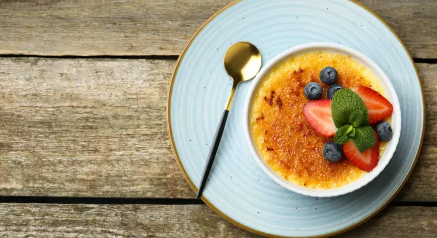 Idealny creme brulee przepis na deser. Karmelizowana skórka, świeże owoce i złota łyżeczka.