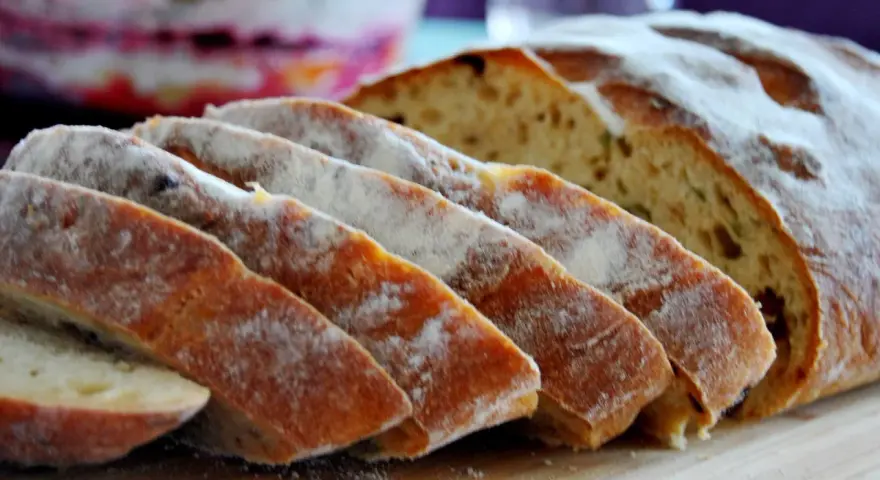 Pokrojony chleb z pomidorami, posypany mąką, leży na desce. W tle widać sałatkę.
