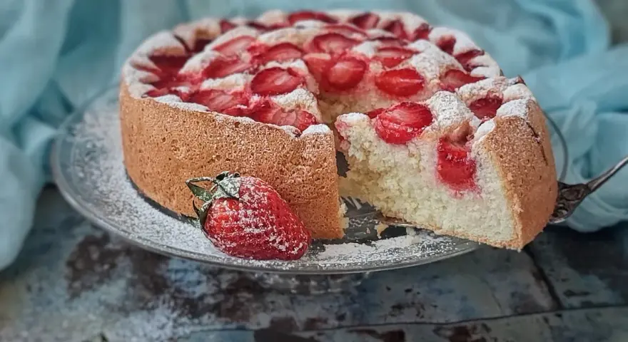 Puszysty biszkopt z truskawkami, posypany cukrem pudrem, kusi apetycznym wyglądem. Idealny na letnie popołudnie.