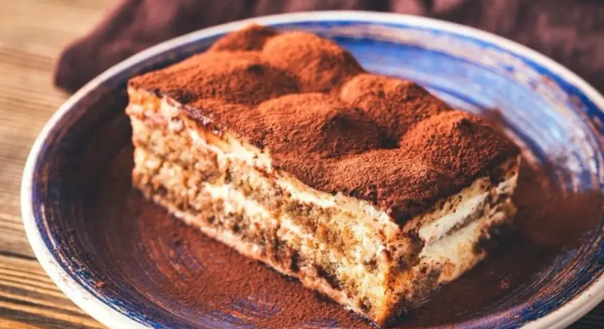 Pyszne tiramisu bez pieczenia, posypane obficie kakao, na niebieskim talerzu. Idealne na deser.