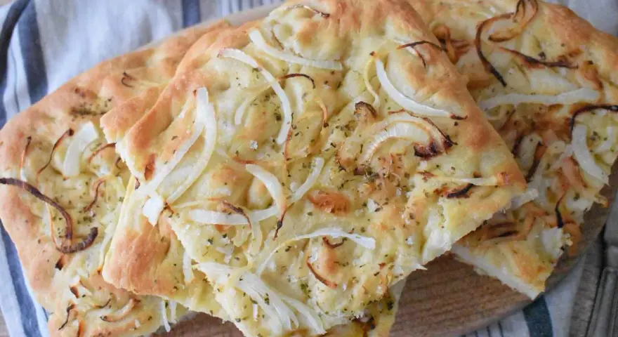Pyszna focaccia z cebulą, posypana ziołami i solą, prezentuje się apetycznie na drewnianej desce.