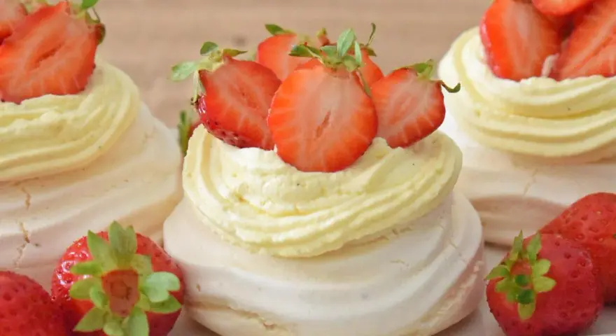 Mini torty pavlova z bitą śmietaną i świeżymi truskawkami.