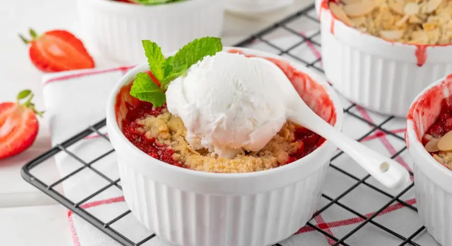 Pyszny crumble z truskawkami w białych kokilkach, ozdobiony świeżymi owocami i miętą.