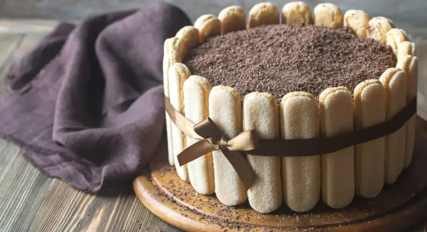 Wykwintny tort tiramisu, otoczony biszkoptami i ozdobiony czekoladową posypką, prezentuje się apetycznie.