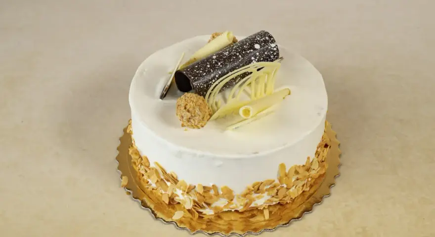 Elegancki tort rafaello z wiórkami migdałowymi, czekoladową rurką i dekoracjami z białej czekolady.