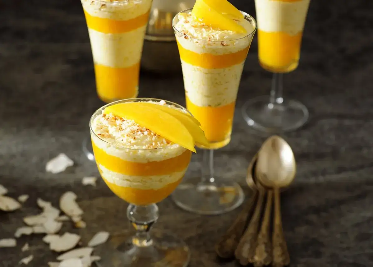 Warstwowy deser z mango i kokosem, podany w kieliszkach, ozdobiony plasterkami mango.