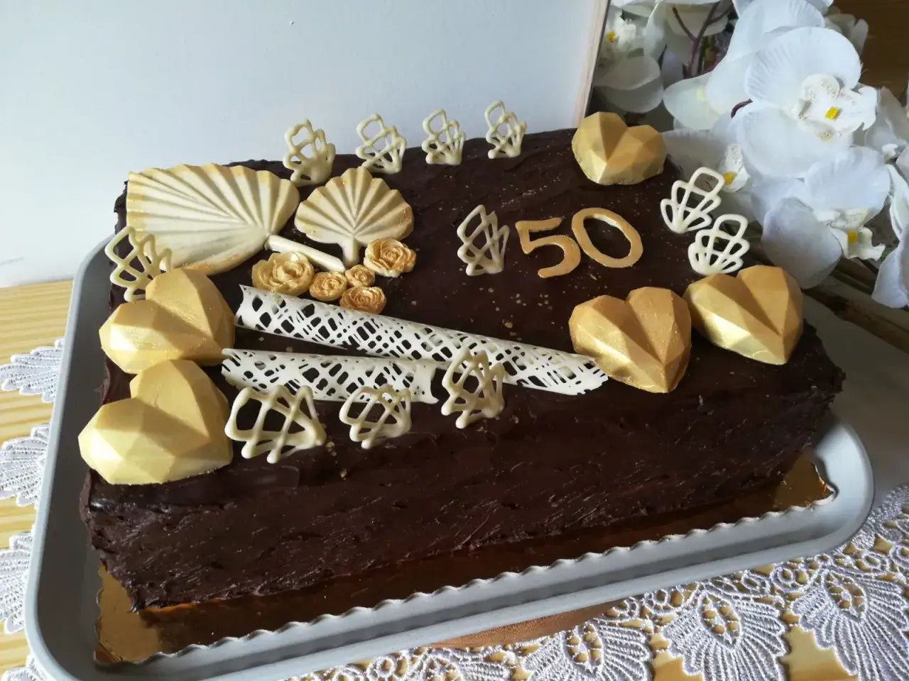 Elegancki tort prostokątny z czekoladą, złotymi sercami i cyfrą 50.