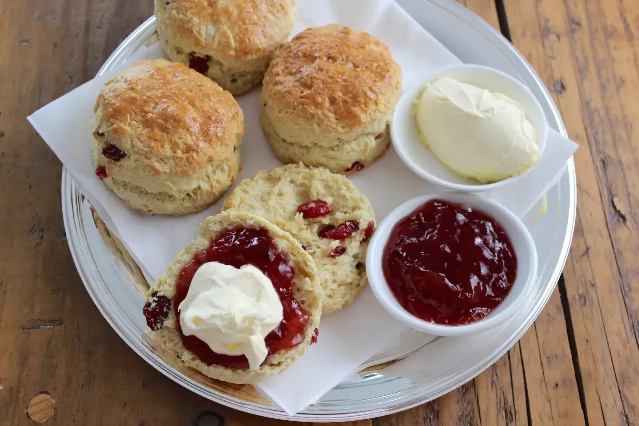 Pyszne bułeczki scones z żurawiną, podane z dżemem i śmietaną. Idealne na podwieczorek.