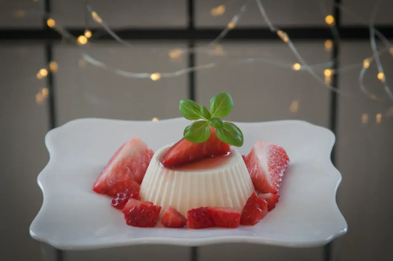 Panna cotta z truskawkami i listkiem bazylii, ozdobiona błyszczącymi światełkami.
