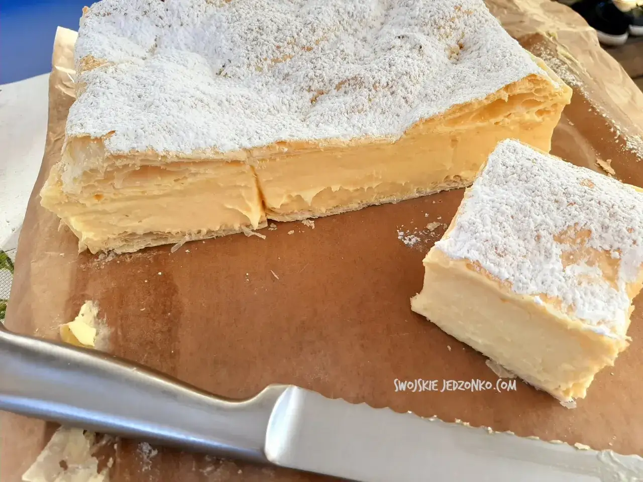 Pyszny krem do krem&oacute;wki, obficie posypany cukrem pudrem, czeka na rozkrojenie. Idealny deser na każdą okazję.