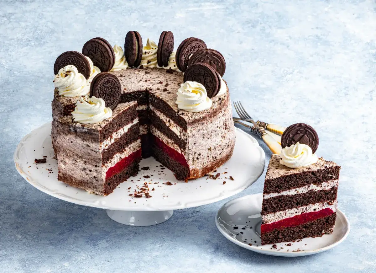 Pyszny tort oreo z warstwami czekoladowego biszkoptu, kremu i czerwonego dżemu. Udekorowany ciasteczkami oreo i bitą śmietaną.