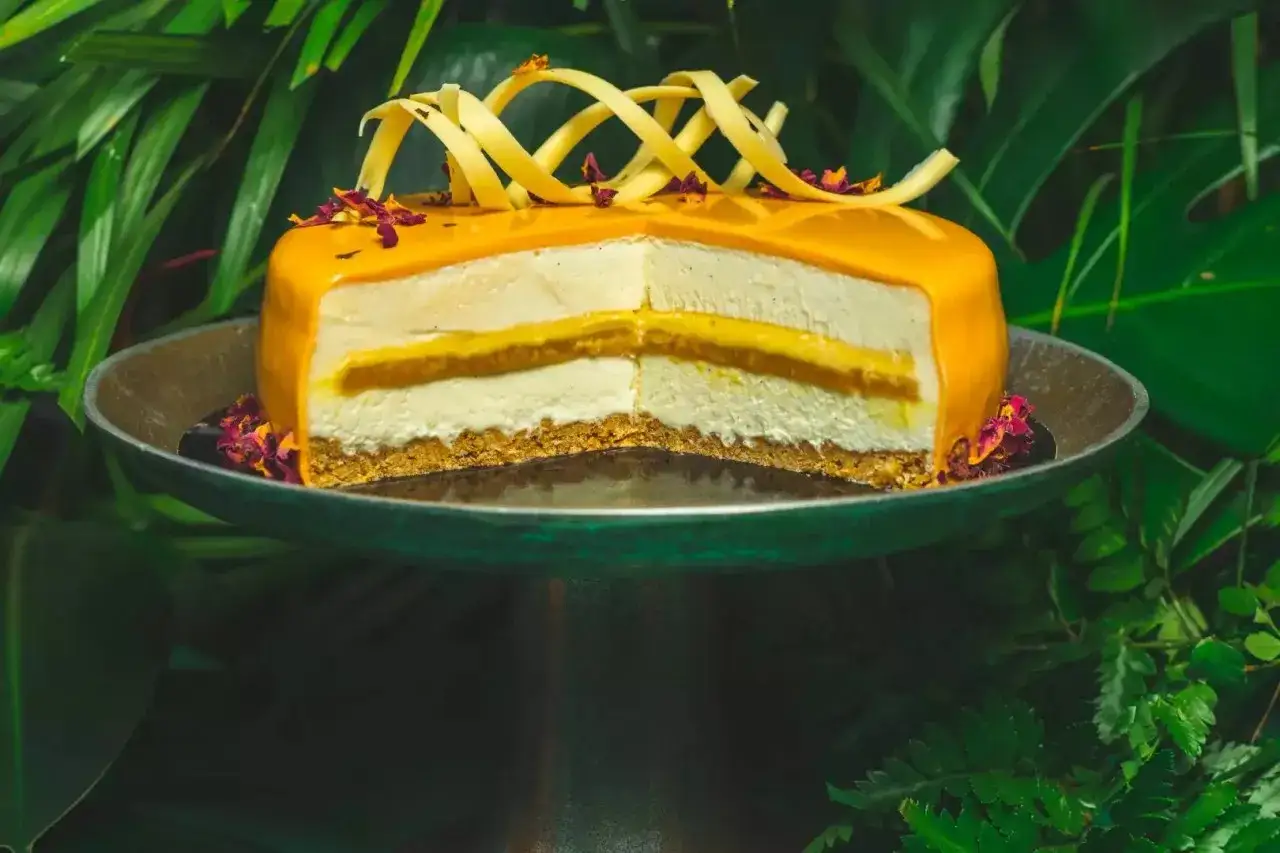 Tropikalny tort mango z kremową warstwą i kruchym spodem, ozdobiony żółtą czekoladą i płatkami róży.