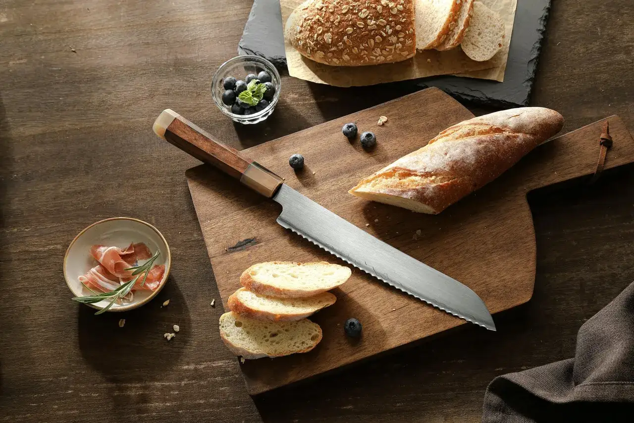 Nóż do chleba z ząbkowanym ostrzem leży obok świeżego pieczywa, jagód i prosciutto. Zastanawiasz się, dlaczego chleb się klei do noża?