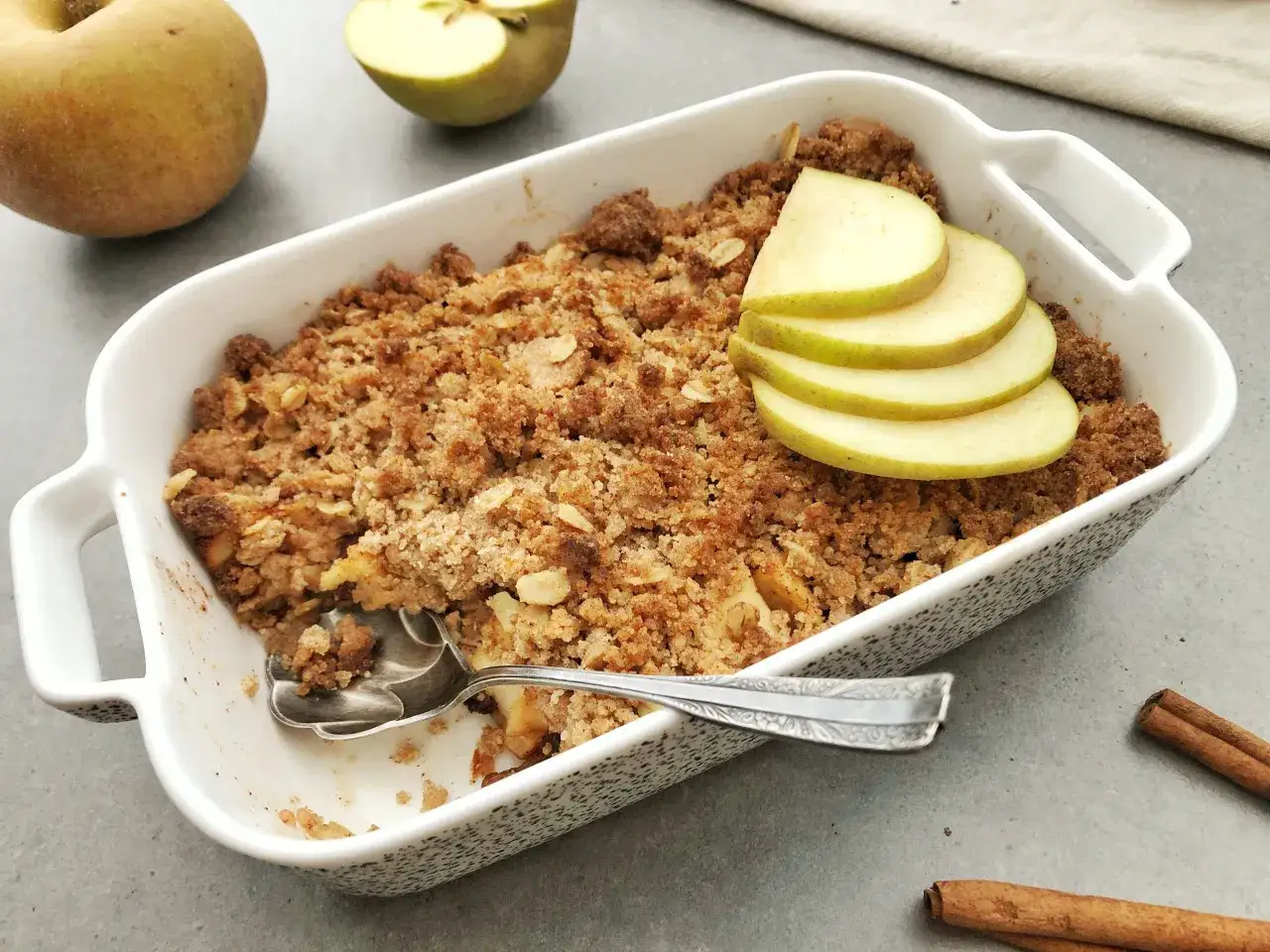 Pyszny crumble z jabłkami, ozdobiony plasterkami jabłka i laskami cynamonu. Idealny deser na jesienne popołudnie.