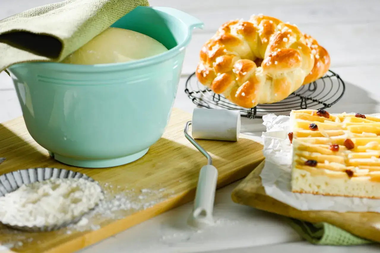 Przygotowania do pieczenia: ciasto na pudding chlebowy w misce, warkocz z cukrem i placek z jabłkami.